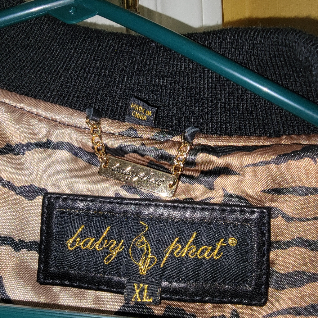 Close-up of a Baby Phat interior label with a gold cat logo and script wordmark stitched into a leopard-print lining